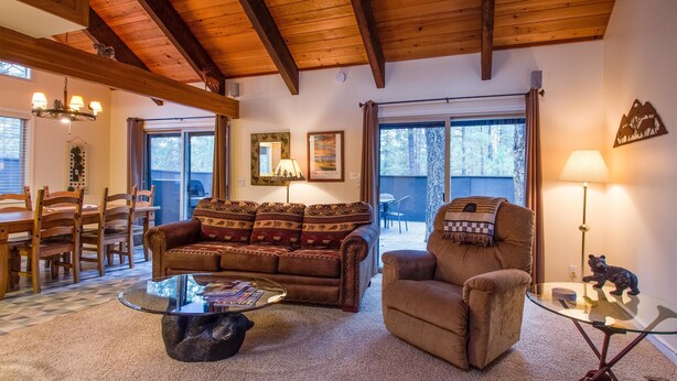 A cozy living room with a wooden ceiling, a sofa, a chair, a glass coffee table, and a dining area with wooden chairs and a table. - Elk Lane 7 (Bend)
