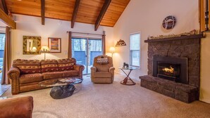 A cozy living room with a stone fireplace, a leather sofa, a coffee table, and a fireplace screen. - Elk Lane 7 (Bend)