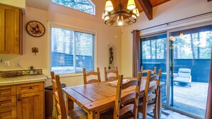 A wooden dining table with chairs, a chandelier, a clock, and a window with blinds. - Elk Lane 7 (Bend)
