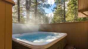 A hot tub with a wooden deck and a view of a forest.