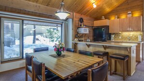 A wooden interior with a dining table, chairs, a kitchen area, and a view of the outside.