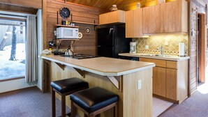 A compact kitchen with wooden cabinets, a black refrigerator, a microwave, and a sink. There are two stools at the counter.