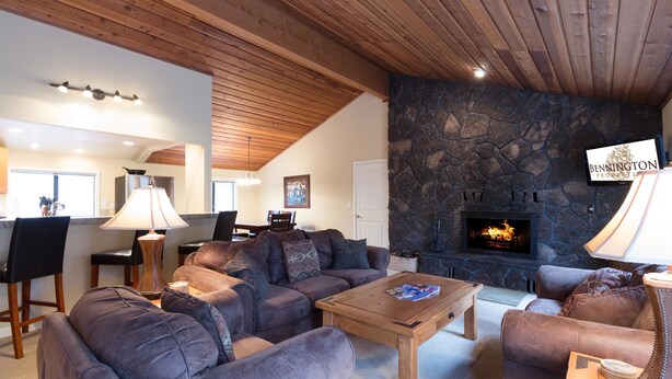 A cozy living room with leather sofas, a stone fireplace, and a dining area with a table and chairs. - Pioneer 7 (Bend)