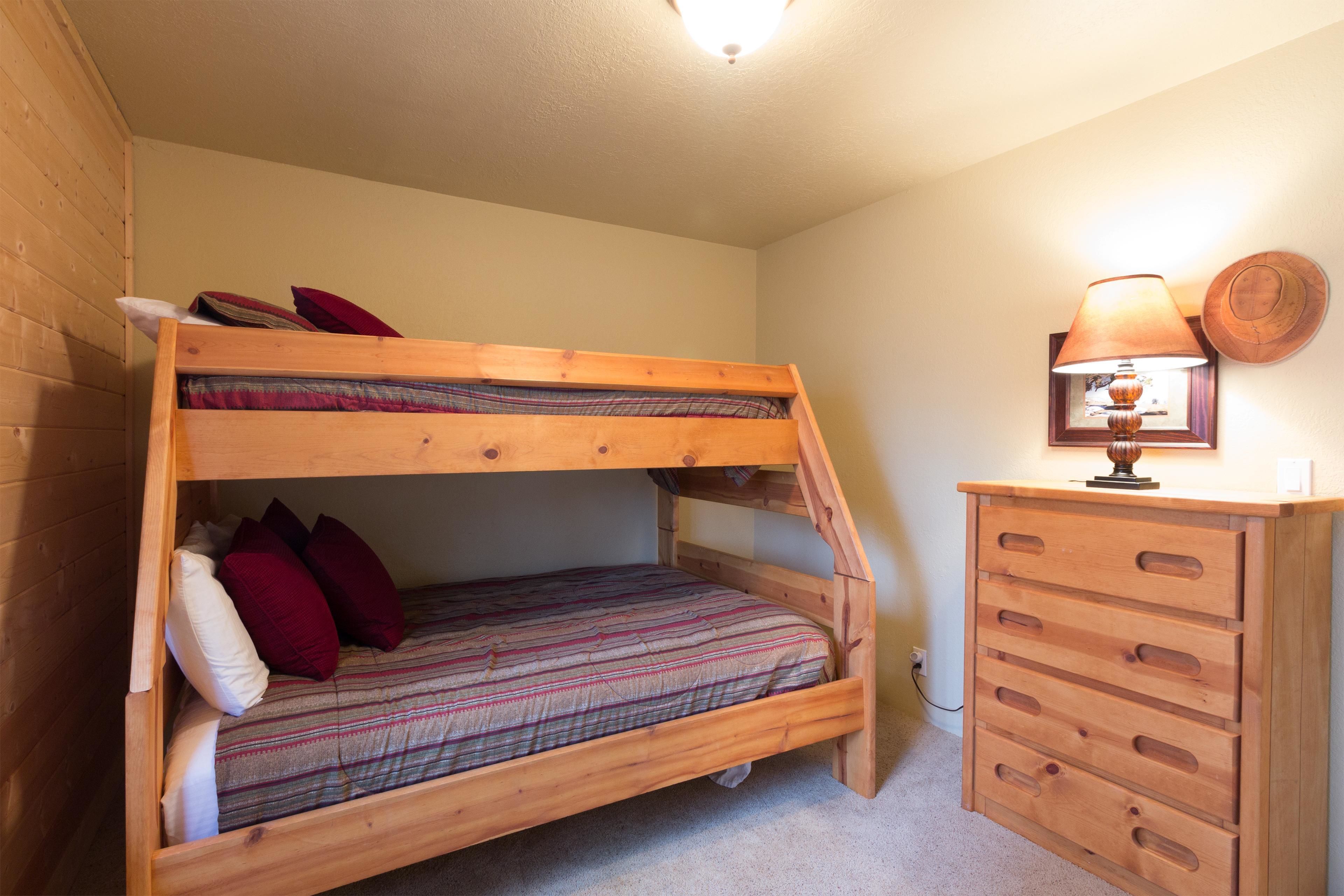 A bunk bed with a wooden dresser beside it, a lamp on the dresser, and a wall-mounted light fixture.