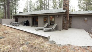 A modern house with a stone chimney, a deck with lounge chairs, and a barbecue area. - Pioneer 7 (Bend)