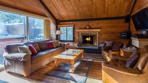 L’intérieur d’un chalet accueillant, avec un plafond en bois, une cheminée, un canapé, une table basse et un téléviseur.