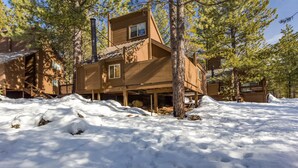 Une cabane en bois avec une cheminée, entourée d’un paysage enneigé et d’arbres.