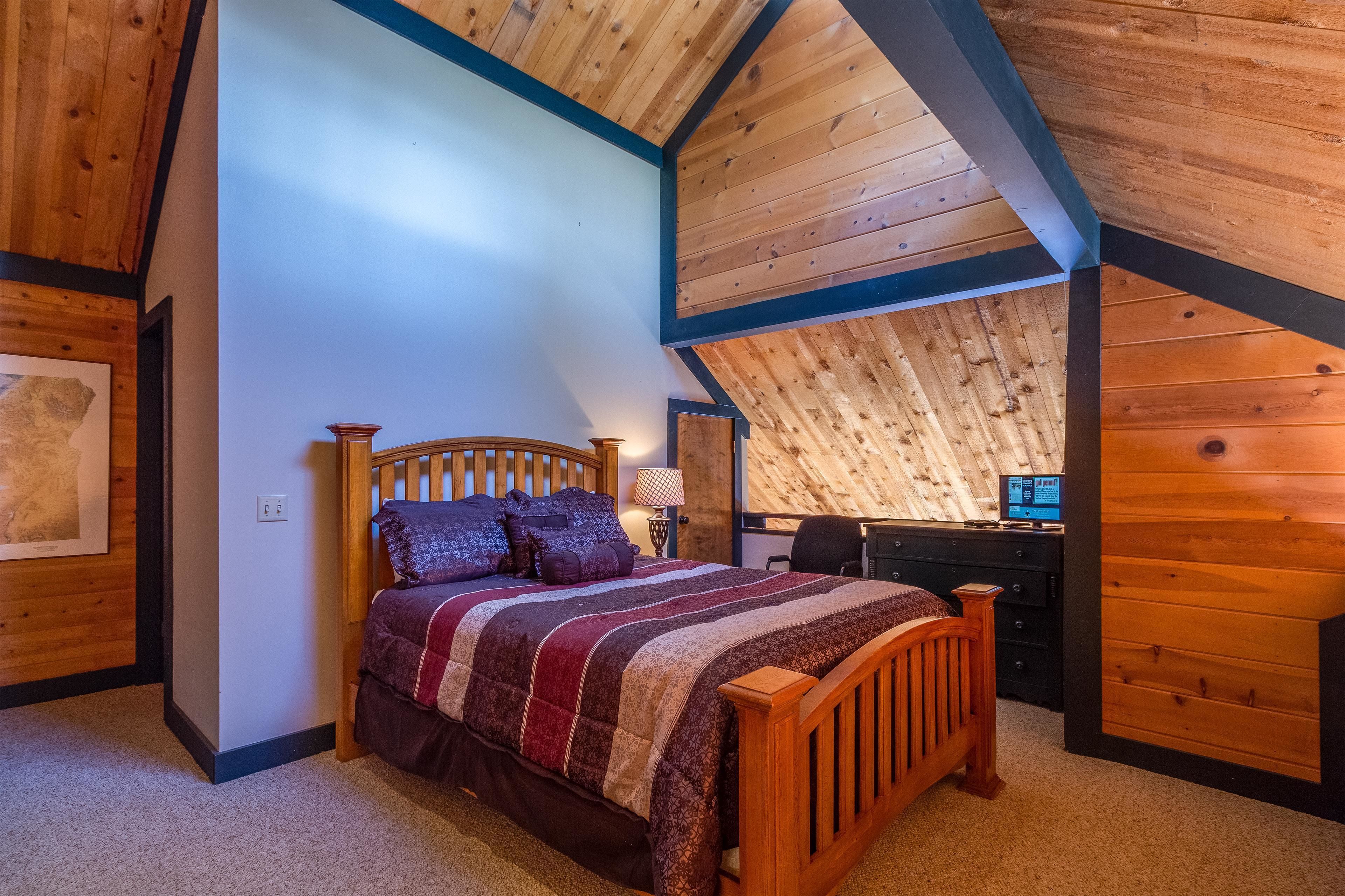 A bedroom with a wooden ceiling, a bed with a striped blanket, a desk, and a chair.