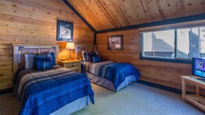 Une chambre confortable de style cabane, avec deux lits, des murs en bois, une grande fenêtre et un téléviseur posé sur une petite table.