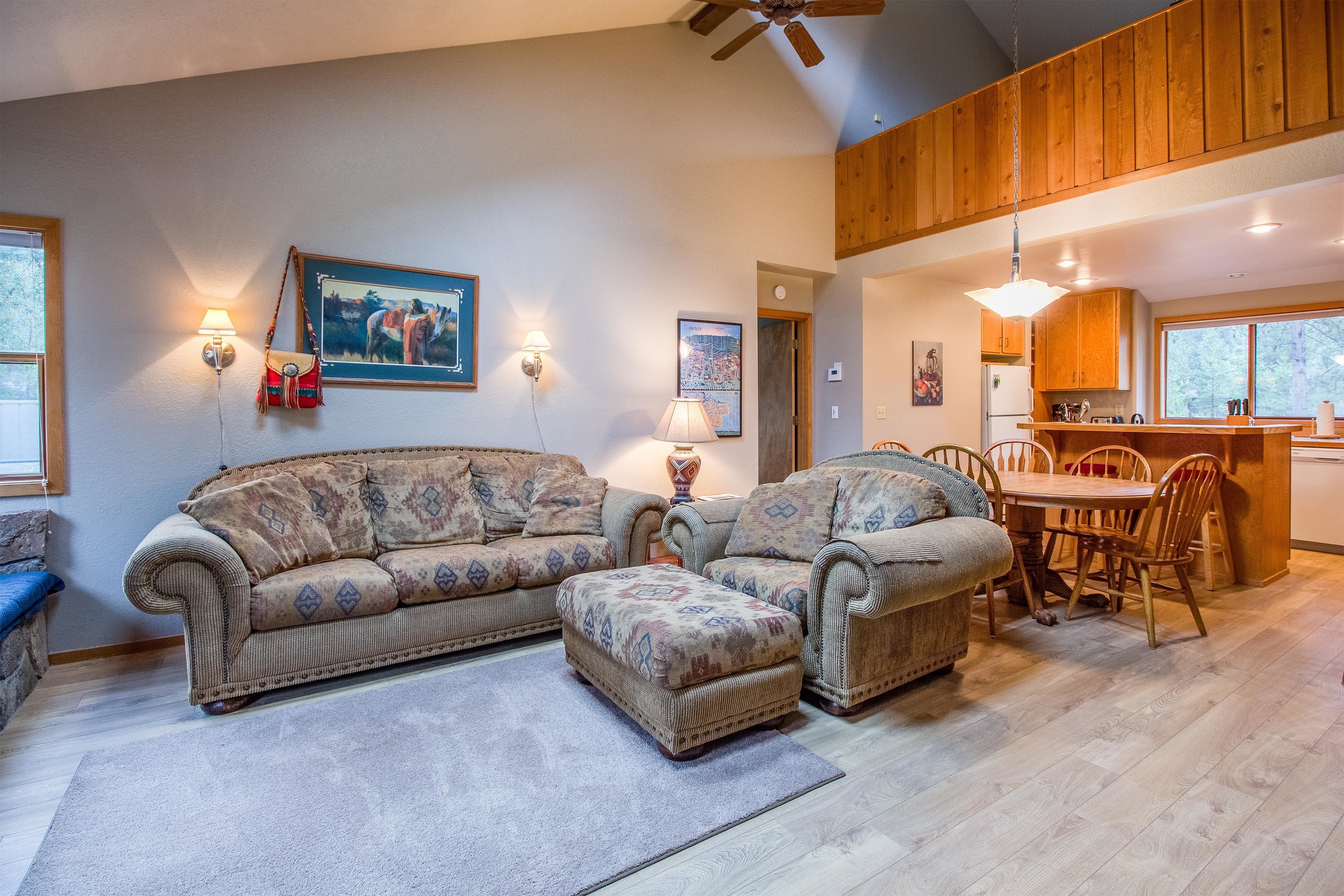 A spacious living room with a large sectional sofa, a dining area with wooden chairs, and a kitchen with wooden cabinets.