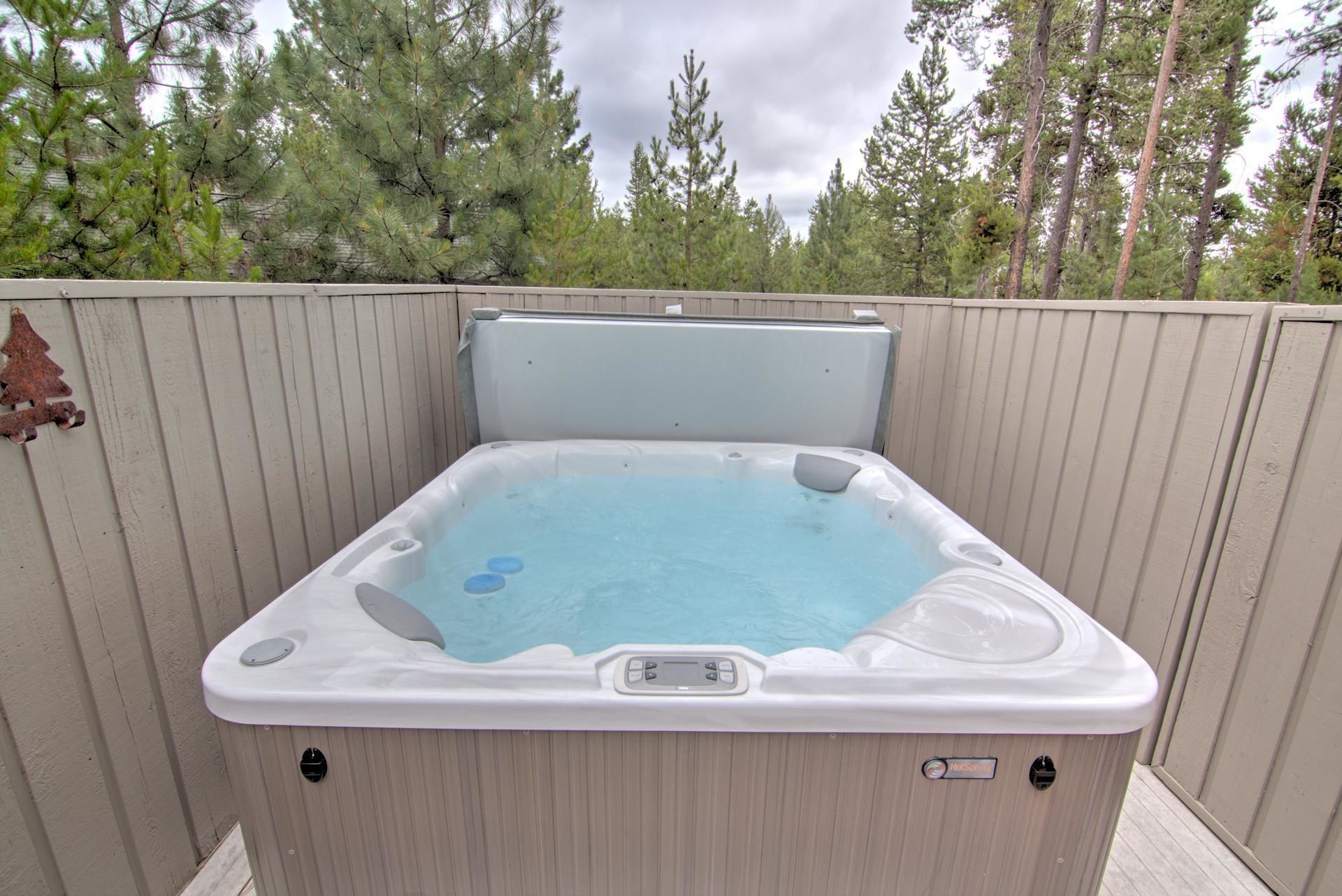 Un bain à remous doté d’un panneau de commande, entouré d’une clôture en bois et d’arbres.