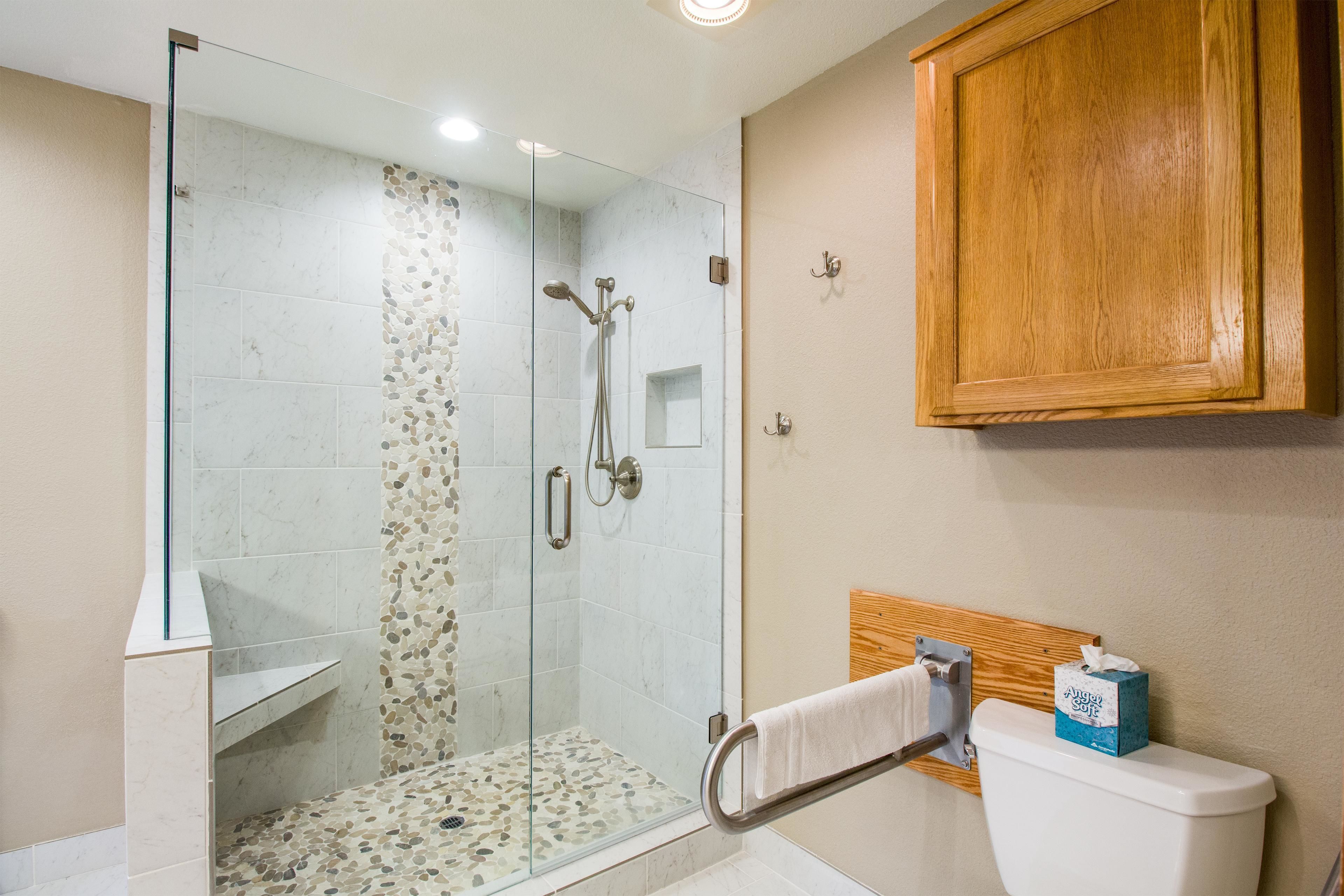 Un baño con ducha vidriada, un armario de madera y un inodoro con caja de pañuelos.
