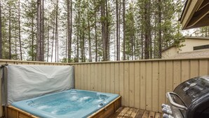 Un bain à remous sur une terrasse en bois, avec en arrière-plan une vue sur de grands arbres.