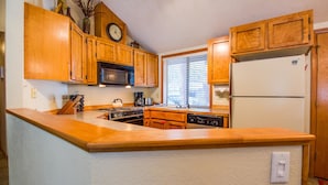 A kitchen with wooden cabinets, a microwave, a refrigerator, and a clock on the wall.