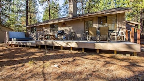 A cabin with a deck, outdoor seating, and a grill area.