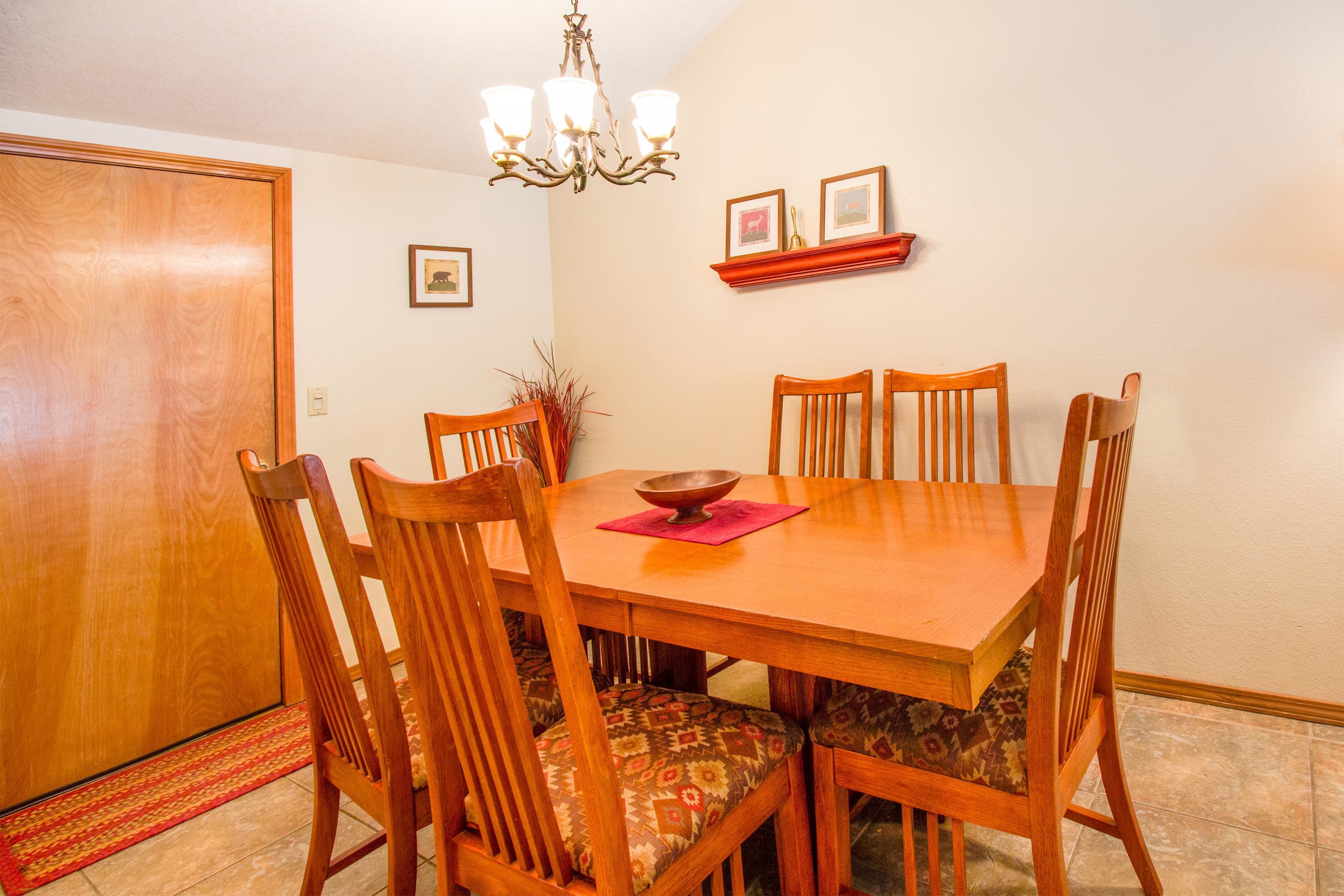 A dining area with a wooden table, six chairs, a chandelier, and a red rug.