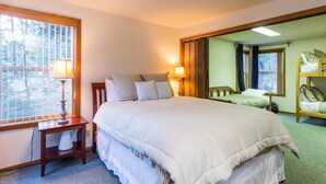 Un dormitorio con una cama grande, lámparas de noche, una mesita de madera y una ventana con persianas.