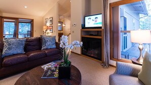 Una sala de estar con un sofá de cuero, una mesa de centro con revistas, una chimenea y un televisor.