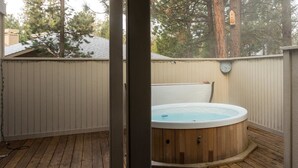 Una terraza de madera con un jacuzzi, cerca viva de madera y un reloj en la cerca.