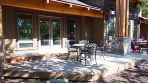 Un patio couvert avec une cheminée en pierre, des sièges d’extérieur et de grandes fenêtres.