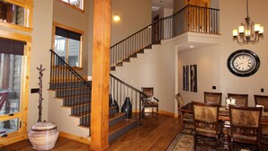 Un intérieur spacieux avec un escalier en bois, un coin repas avec des chaises et une grande horloge murale.
