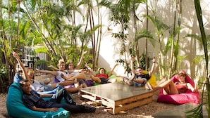 A group of people sitting on bean bags and cushions in a sunlit outdoor area surrounded by tall palm trees. - Down Under Hostels on Harriet (Darwin)