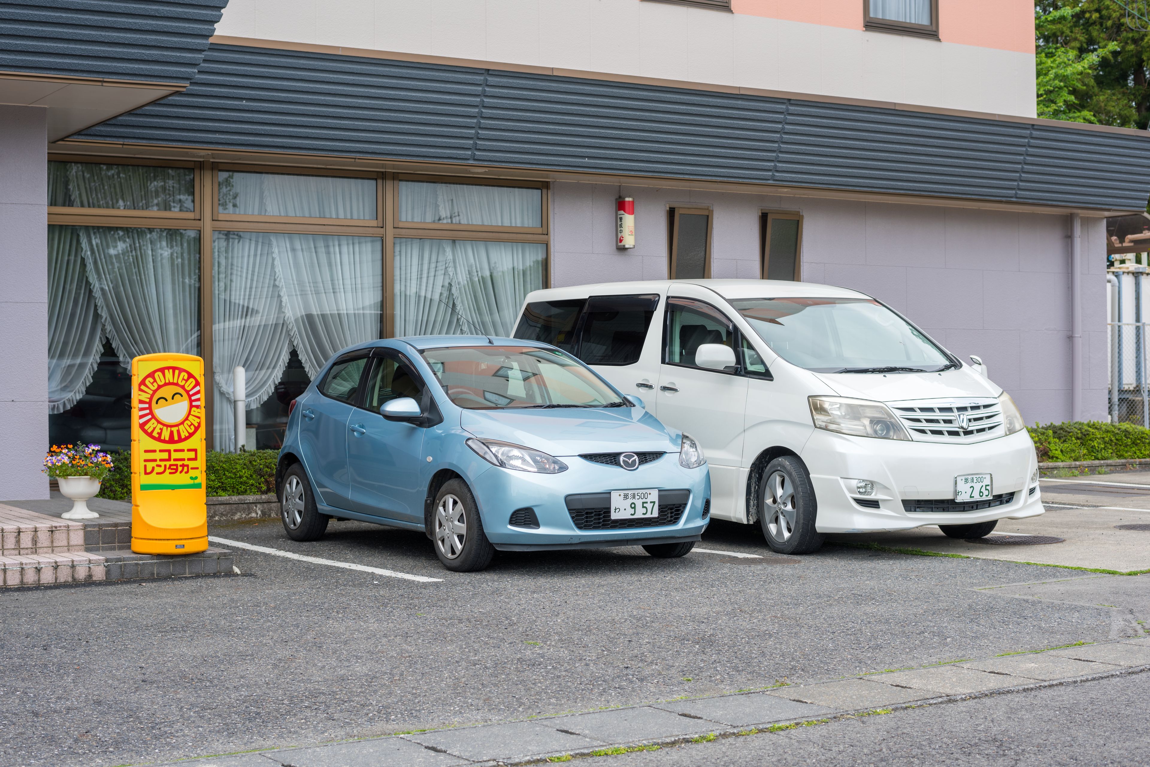 Two parked cars in front of a building with large windows and a fire extinguisher mounted on the wall.