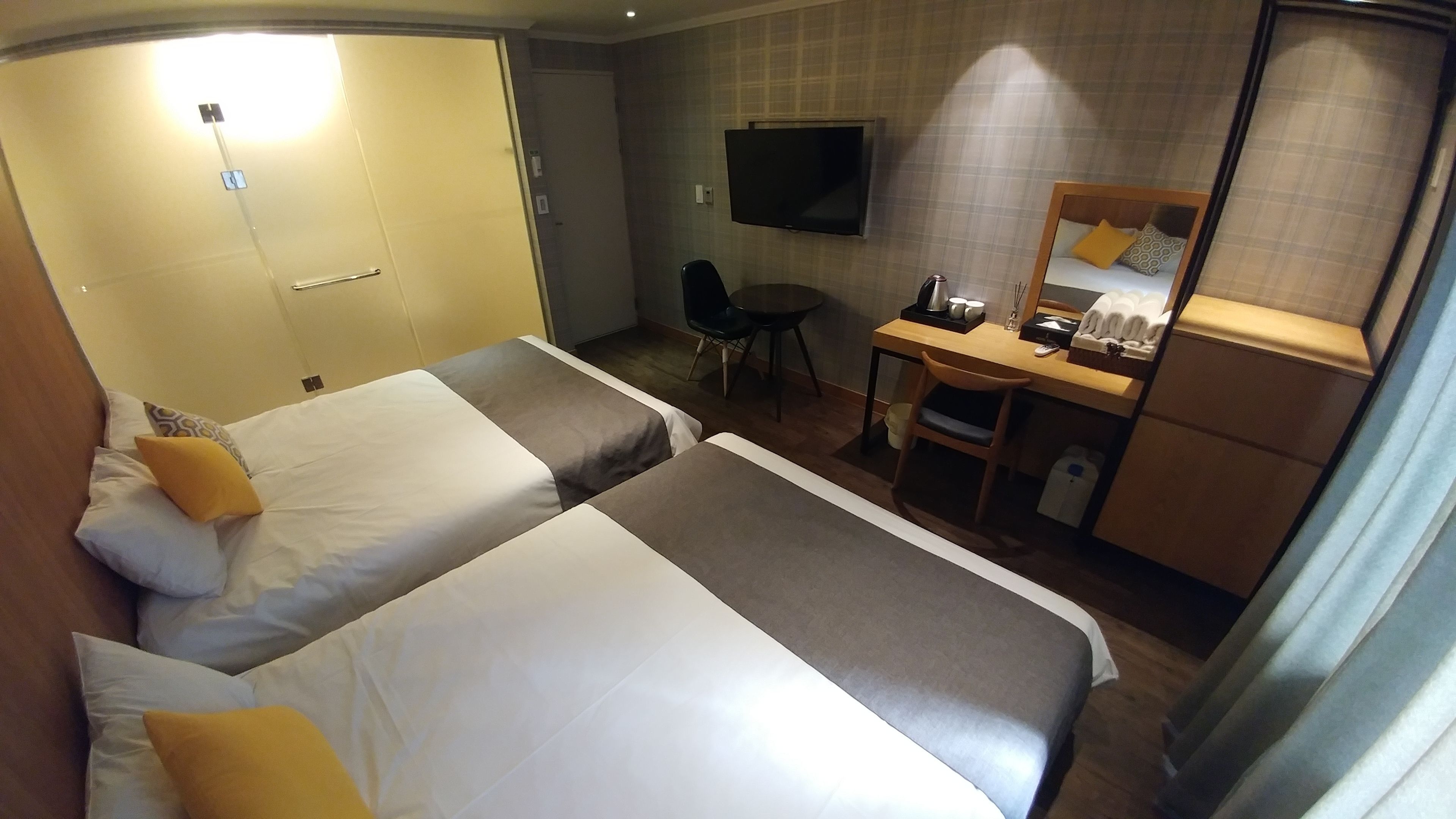 A hotel room with two beds, a desk, a chair, a TV, and a bathroom.