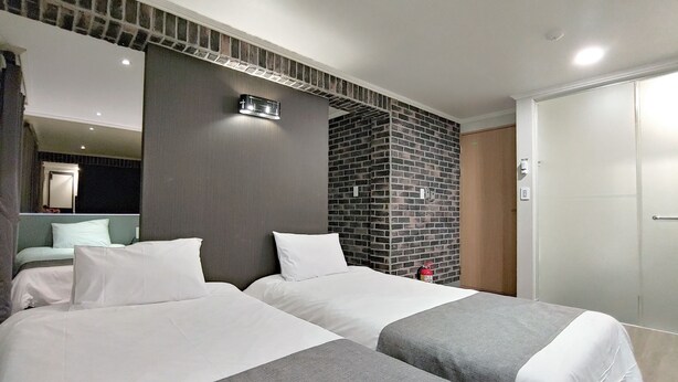A hotel room with two beds, a brick accent wall, a mirror, and a door. - Hotel Tong Yeondong Jeju (Jeju City)