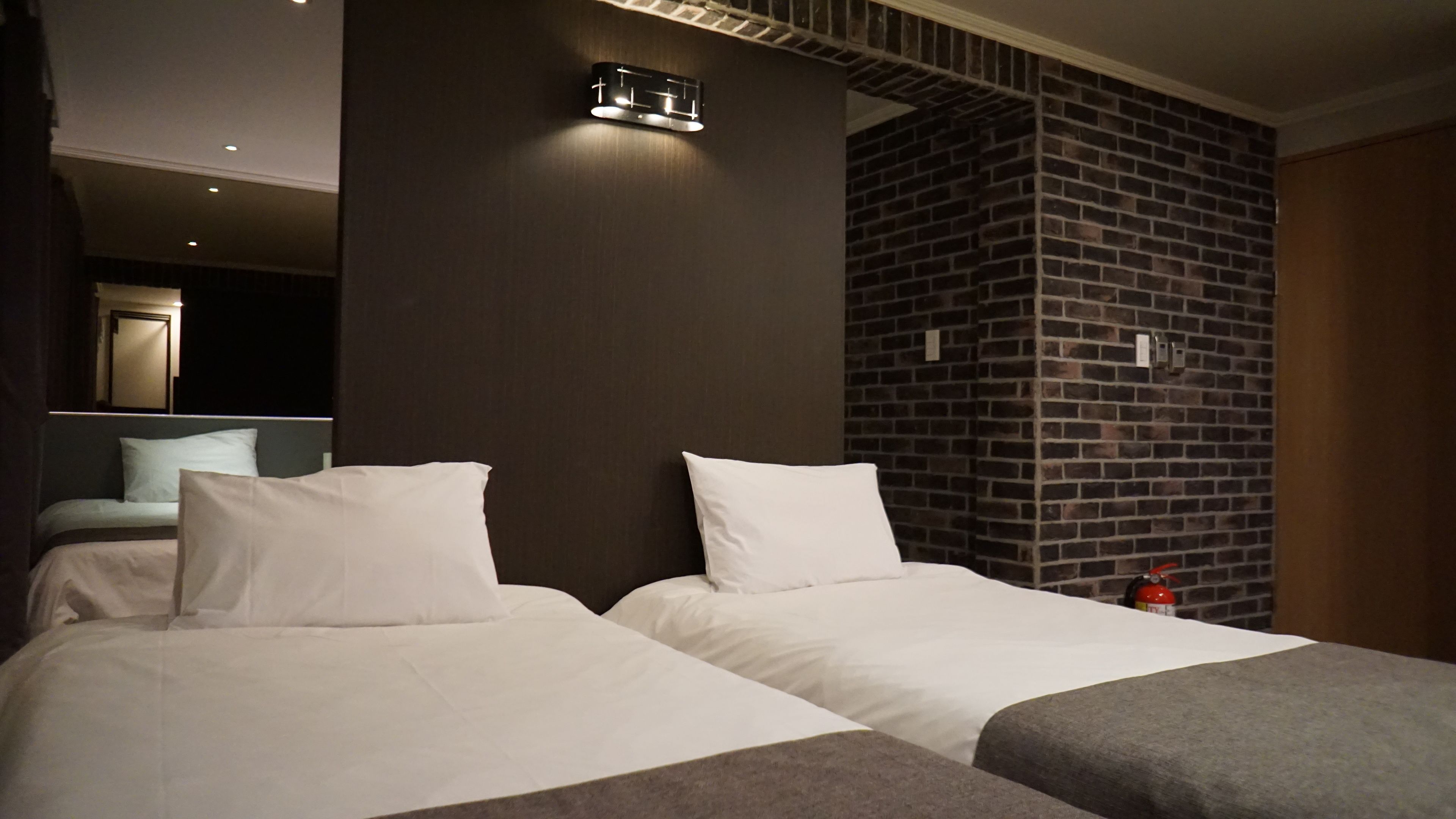 A hotel room with two beds, a brick accent wall, and a modern light fixture.