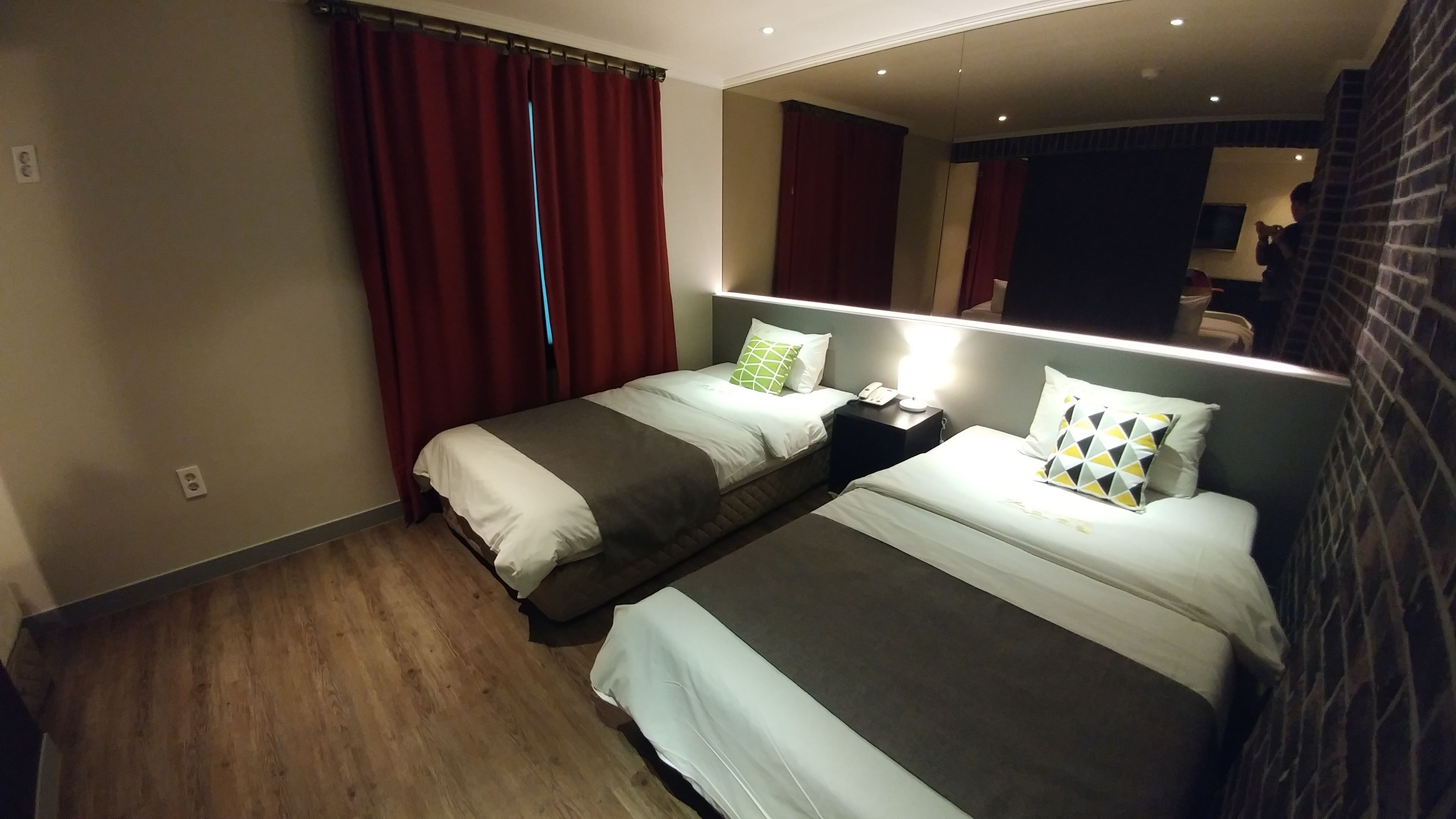 A hotel room with two beds, a nightstand, a mirror, and red curtains.