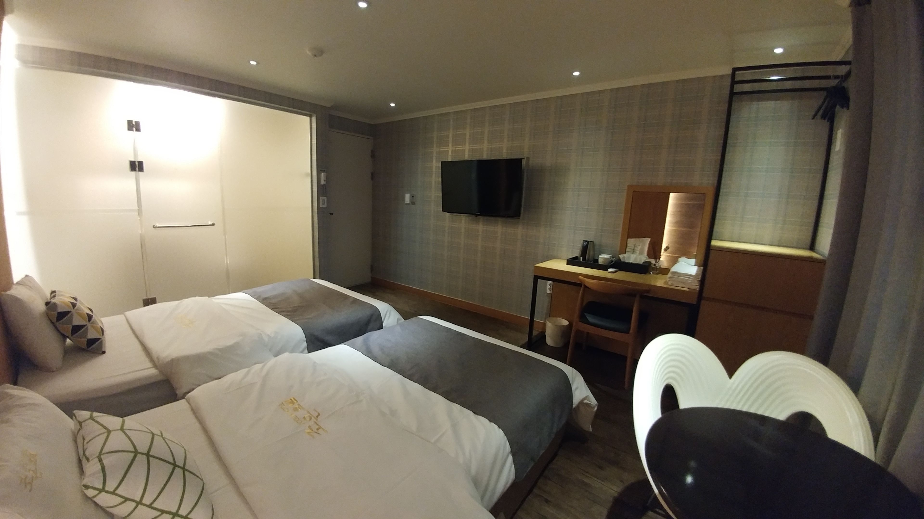 Une chambre d’hôtel avec deux lits, un bureau, une chaise, une télévision et un miroir.