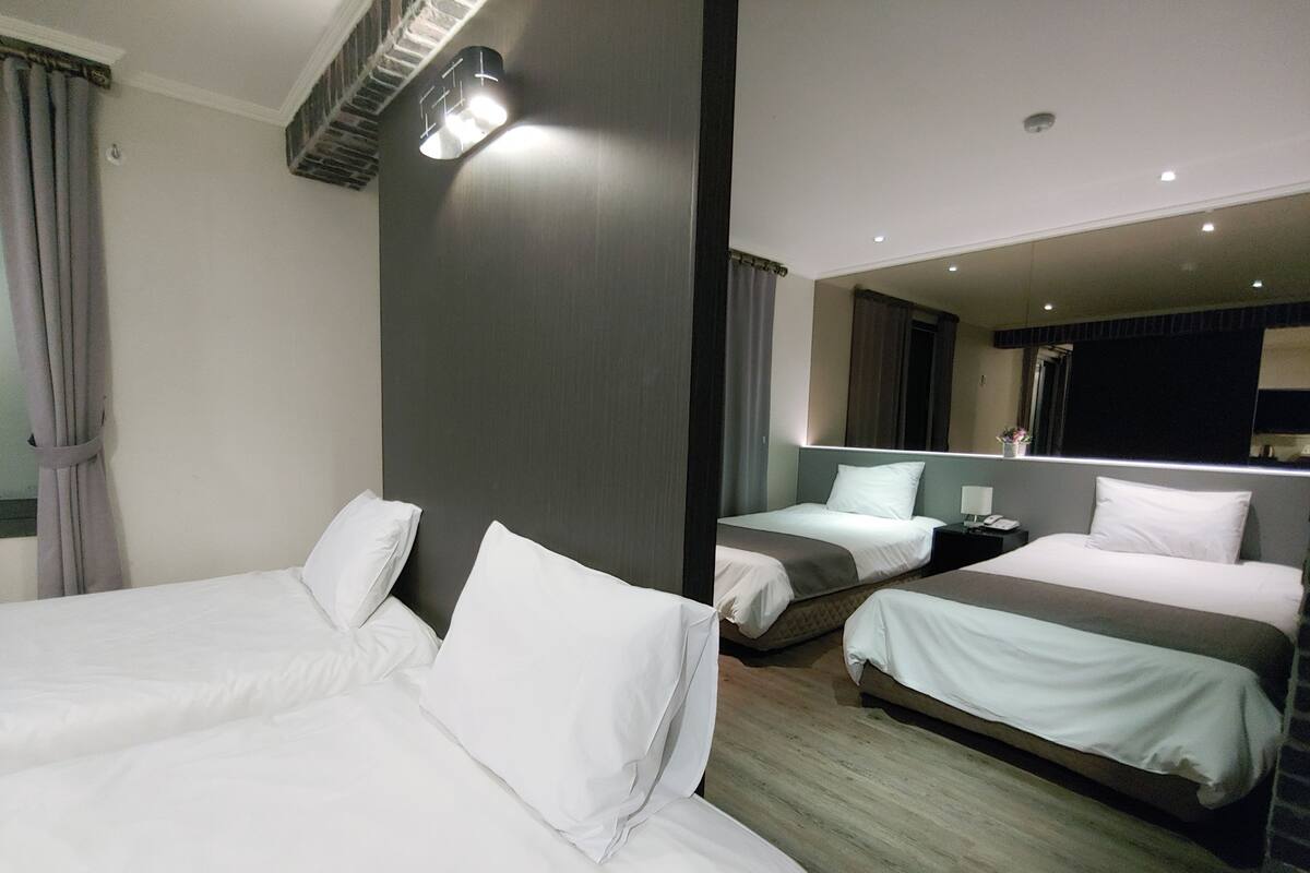 A hotel room with two beds, a large mirror, and a modern light fixture.