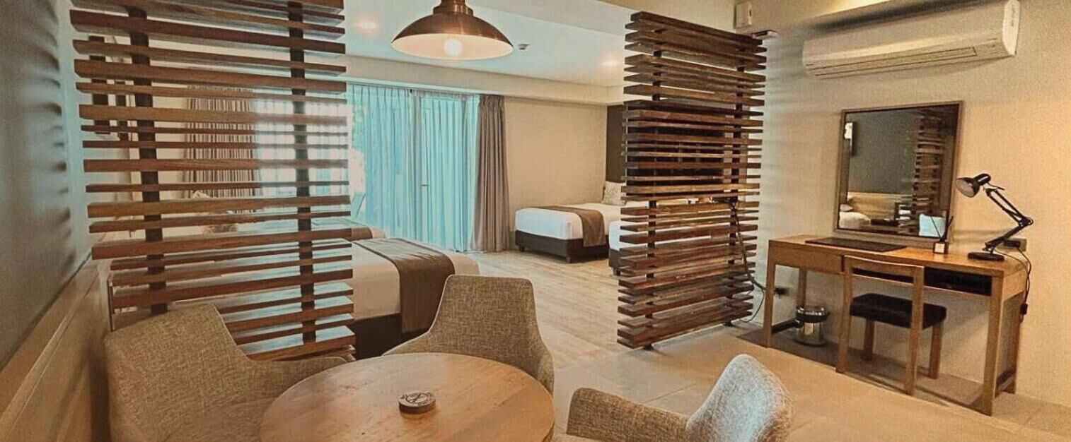 A hotel room with a bed, a desk with a lamp, a chair, a round table, and a large window with curtains.