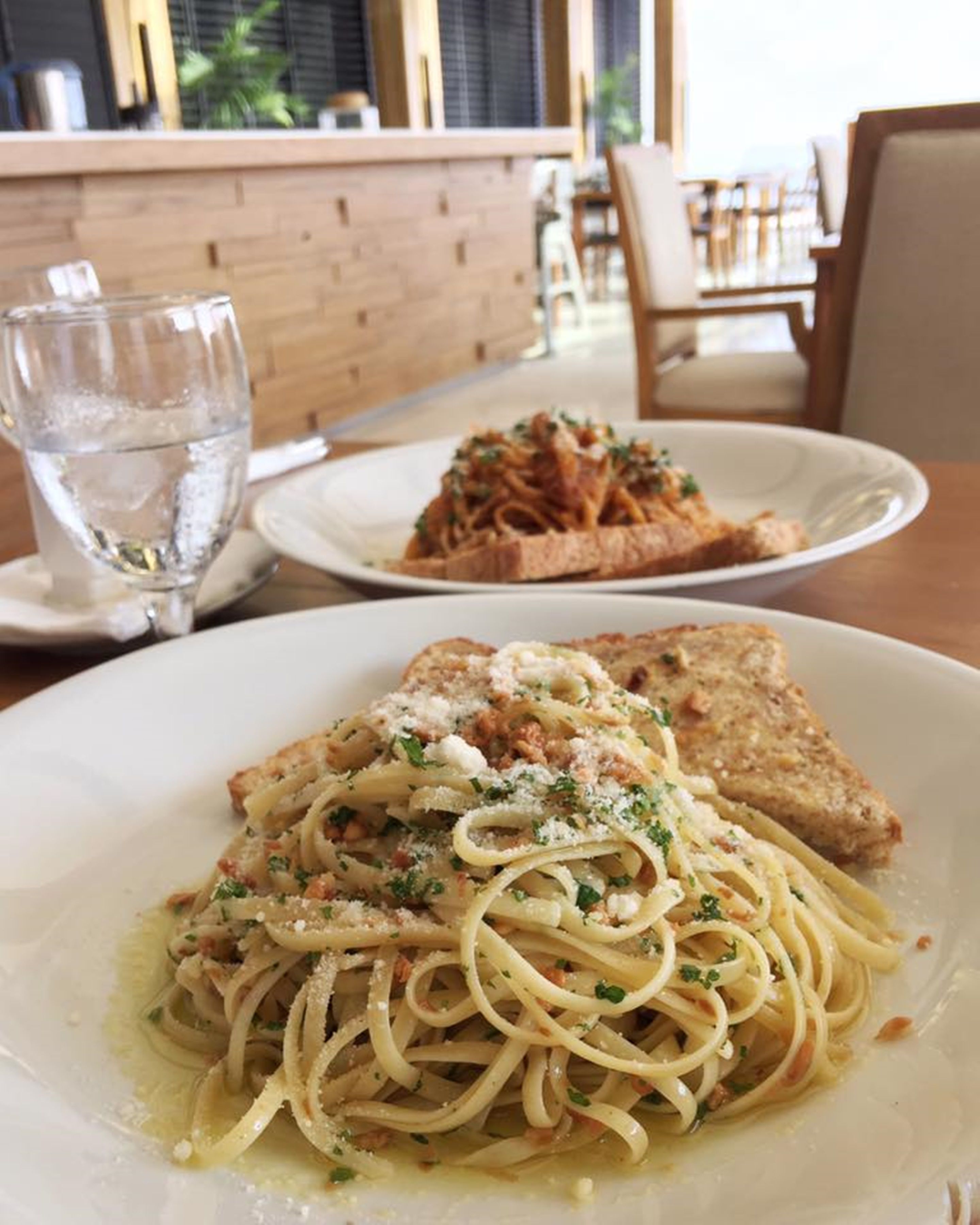 A dining table with two plates of pasta and a glass of water.