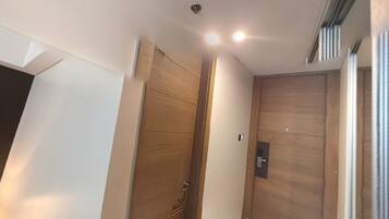 A hallway with a wooden door, a light switch, and a vent on the wall.