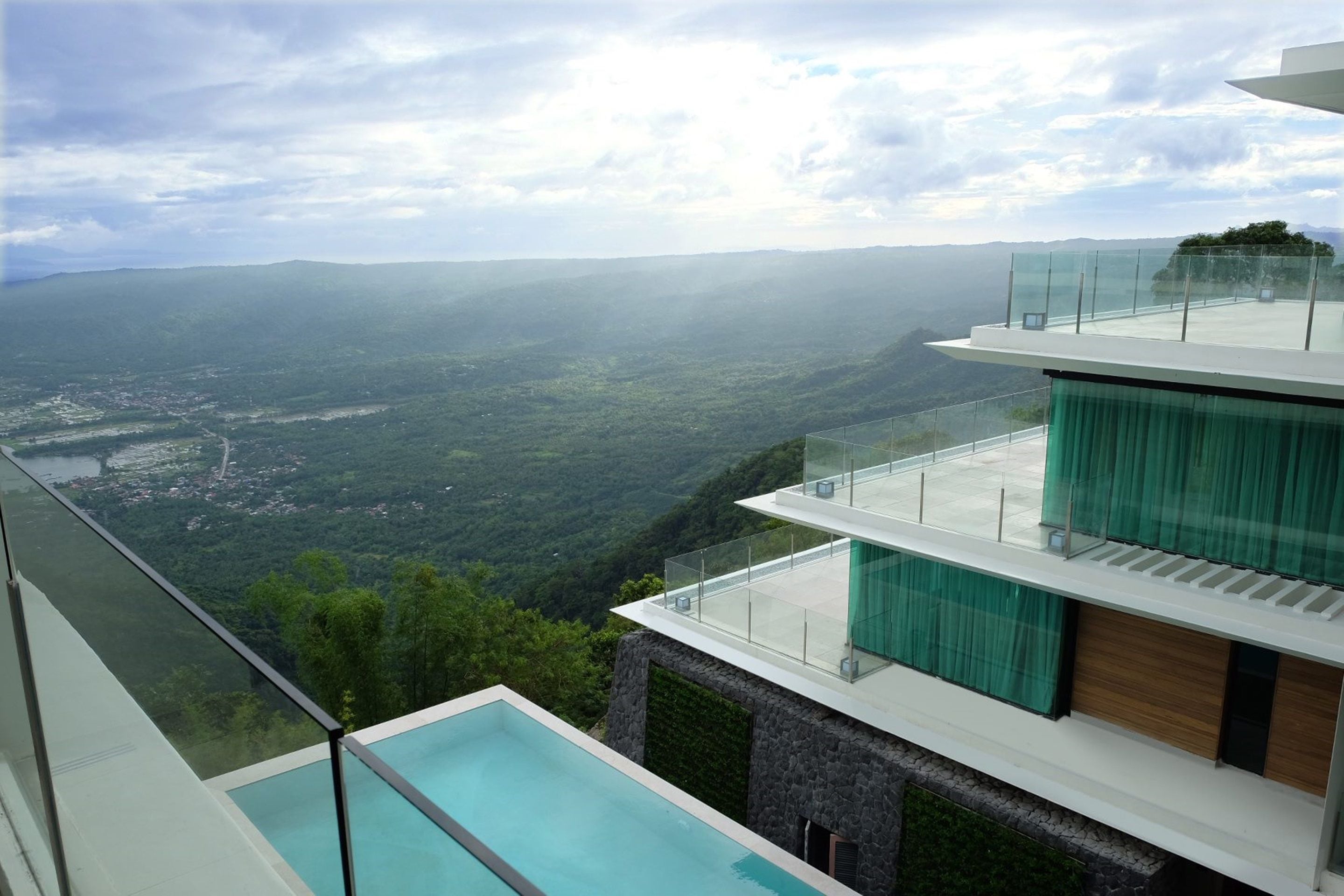 A modern multi-story building with a glass balcony overlooking a valley.
