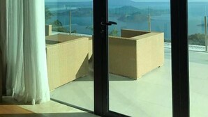 A room with a large sliding glass door leading to a balcony with wicker furniture and a view of the sea and mountains. - Escala Tagaytay (Tagaytay)