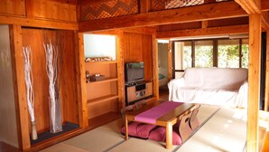 Ein traditioneller Holzraum mit Tatami-Böden, einem Fernseher, einer Couch und einem kleinen Tisch mit Kissen.