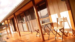 Eine hölzerne Veranda mit Klappstuhl und Tisch, großen Fenstern und Blick auf die Umgebung.