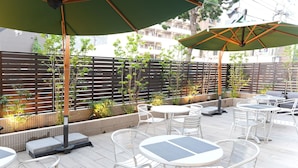 A patio area with outdoor seating, including round tables and chairs, shaded by large umbrellas. - The BREAKFAST HOTEL Fukuoka Tenjin (Fukuoka)