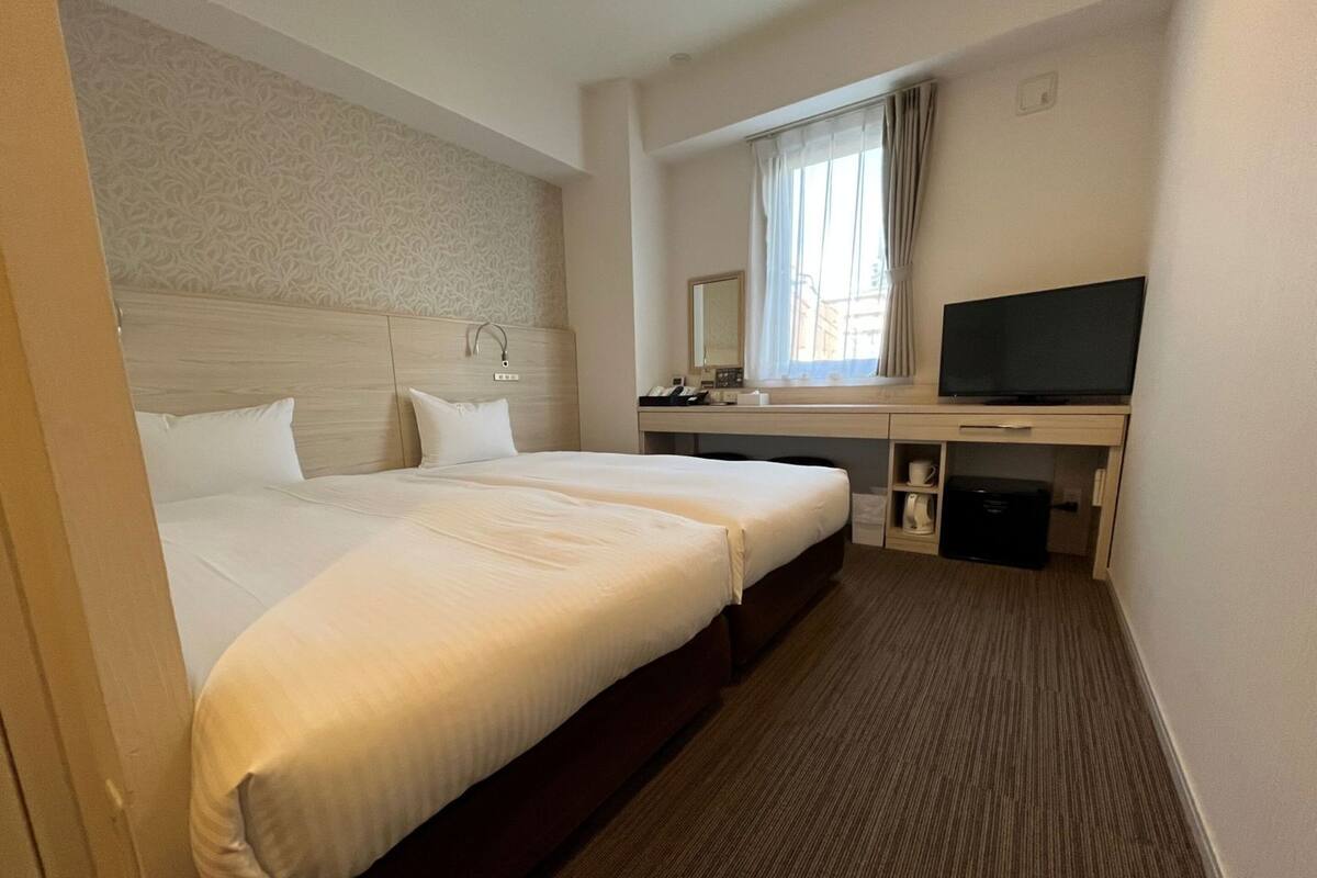 Une chambre d’hôtel avec un grand lit, un bureau avec une télévision, une fenêtre avec des rideaux et une tête de lit agrémentée d’un miroir.