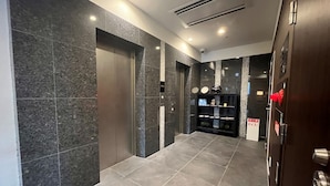 A modern elevator with a digital display, a hallway with dark tiled walls and floors, and a door with a red emergency button. - The BREAKFAST HOTEL Fukuoka Tenjin (Fukuoka)
