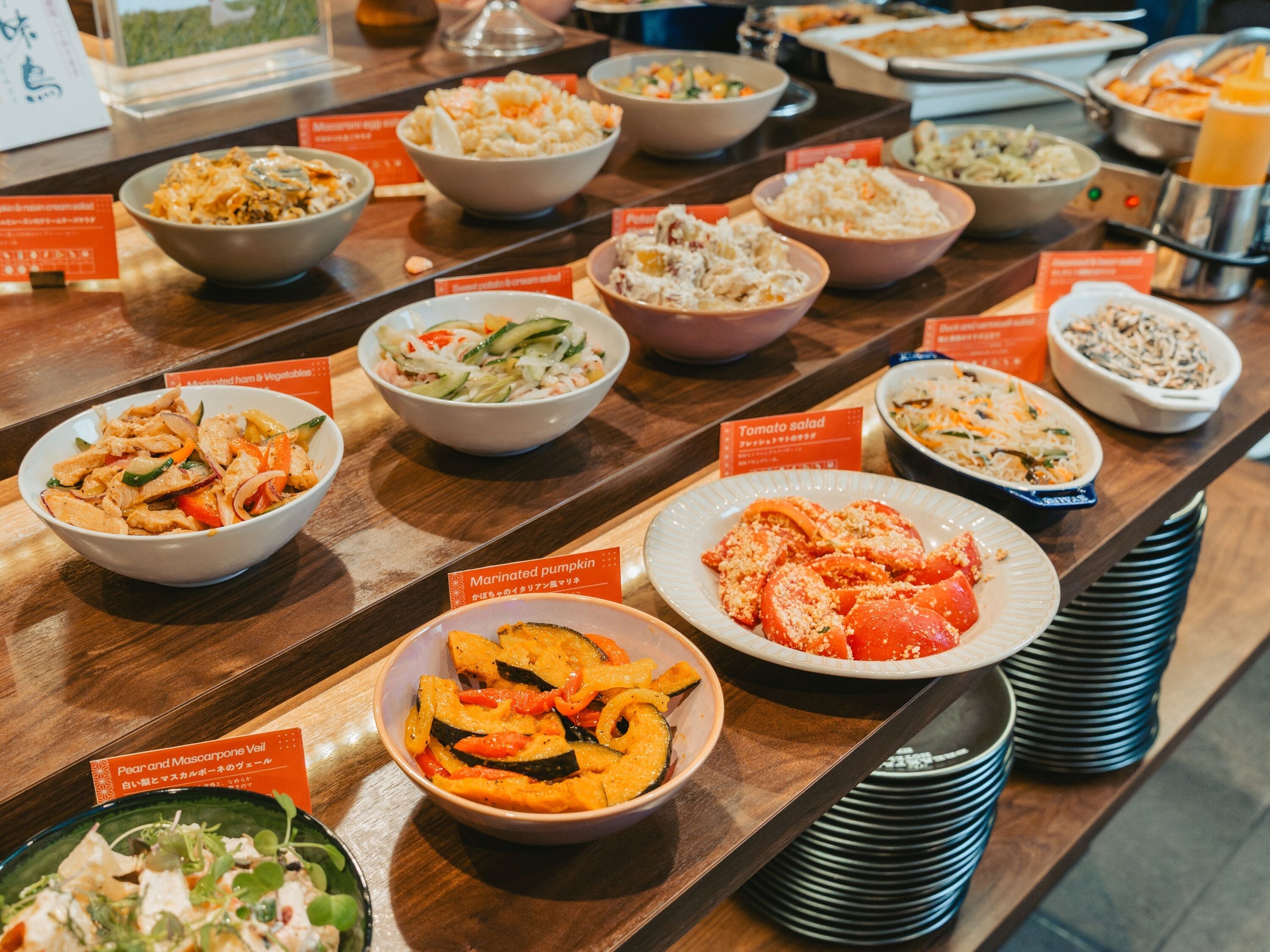A buffet with various dishes including marinated pumpkin, tomato salad, and a dish with chicken and vegetables.