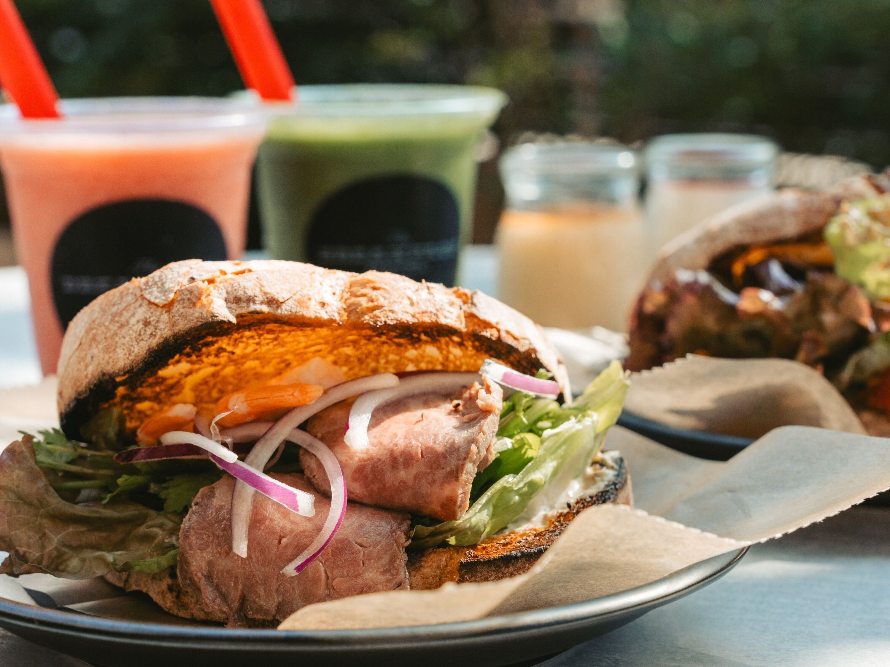 A sandwich with lettuce, red onion, and a toasted bread base, accompanied by a drink in a glass with a straw.
