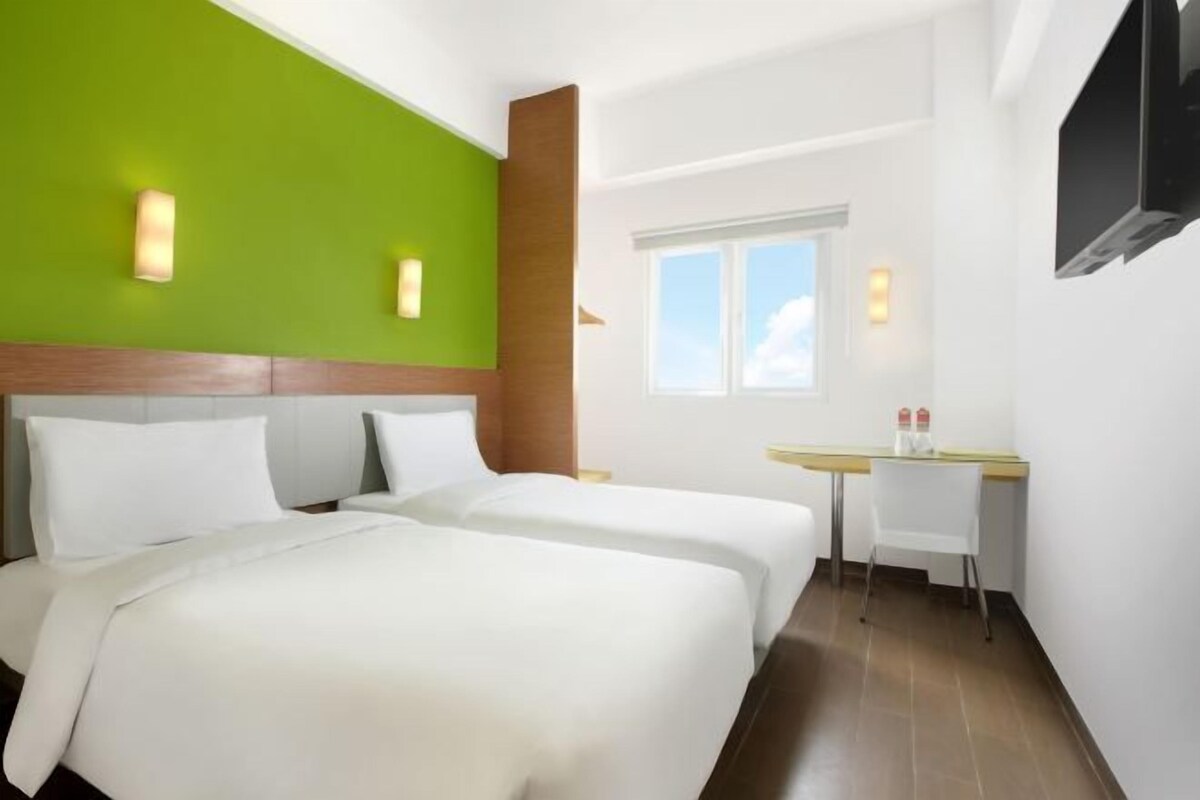 A hotel room with two beds, a desk, and a window.