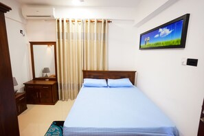 Un dormitorio con cama, mesita de noche, espejo, ventana con cortinas y televisor montado en la pared.