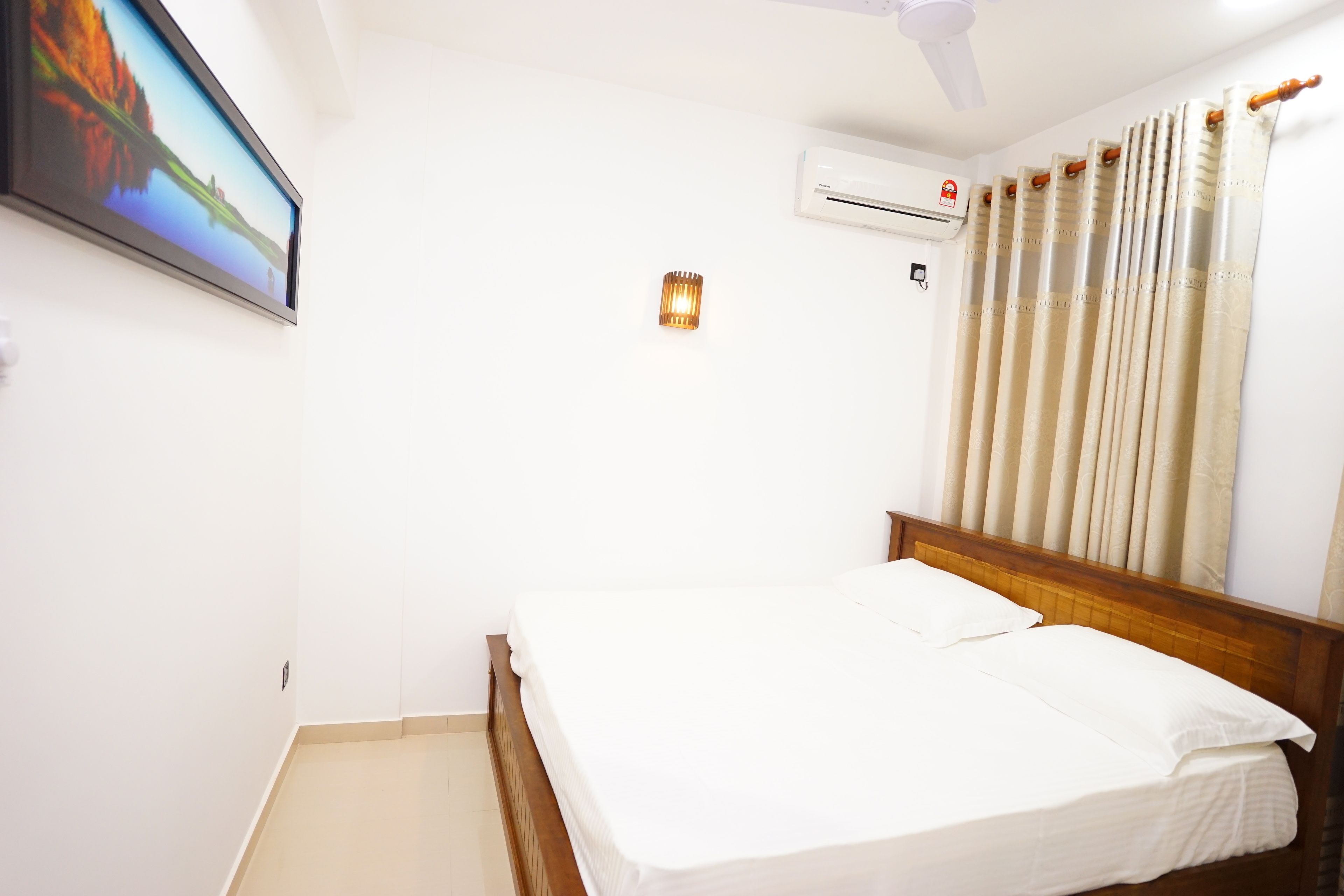 A bedroom with a bed, an air conditioner, a ceiling fan, and a window with curtains.