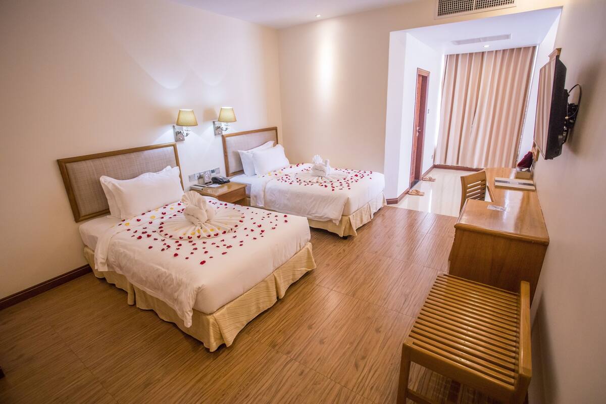 Habitación de hotel con dos camas, un escritorio, una silla, un televisor y un ventanal con cortinas.