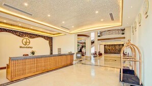 A spacious lobby with a reception desk, a decorative wall with a logo, and a grand staircase. - Golden Hotel (Mandalay)